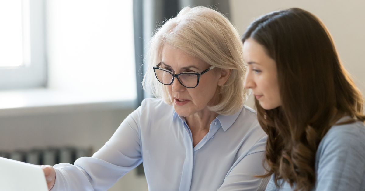 an experienced female professional showing a younger how to do something to illustrate Elevating Your Career: The Transition from Management to Leadership with a Career Coach